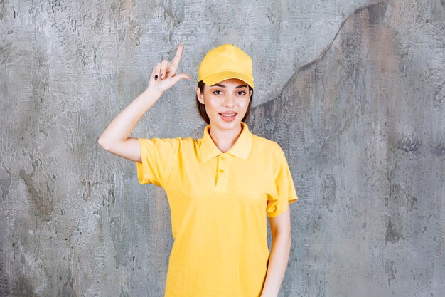 Agente de servicio femenino en uniforme amarillo de pie sobre un muro de hormigón y mostrando arriba.