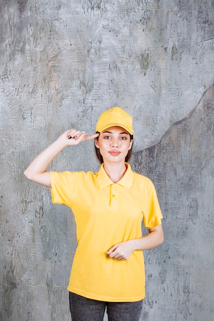 Agente de servicio femenino en uniforme amarillo de pie sobre muro de hormigón parece pensativo.
