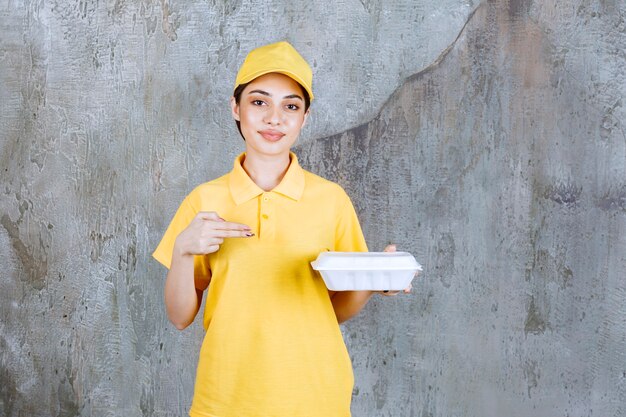 Agente de servicio femenino en uniforme amarillo sosteniendo una caja de comida para llevar de plástico.