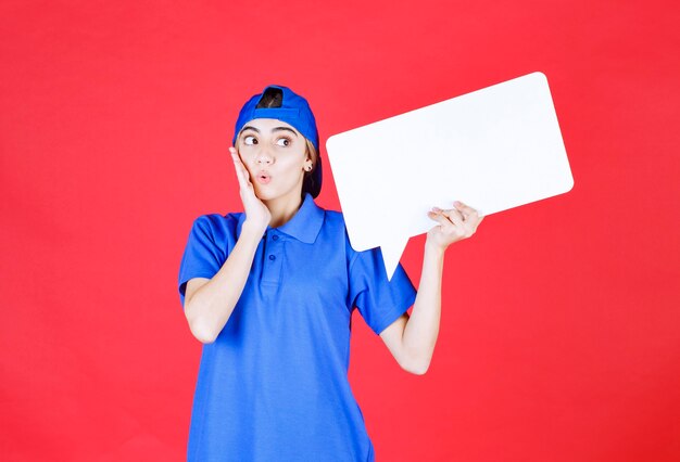 Agente de servicio femenino en uniforme azul sosteniendo un mostrador de información rectangular y parece confundido o emocionado.