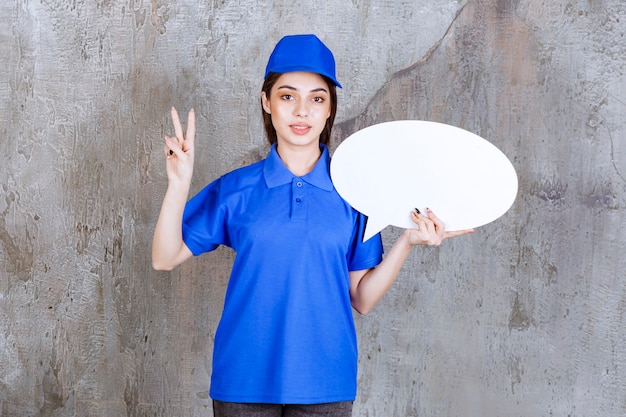 Foto gratuita agente de servicio femenino en uniforme azul sosteniendo un tablero de información ovale y mostrando un signo de mano positivo.