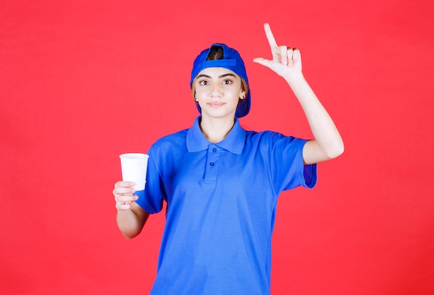 Agente de servicio femenino en uniforme azul sosteniendo una taza de bebida desechable y teniendo una buena idea.
