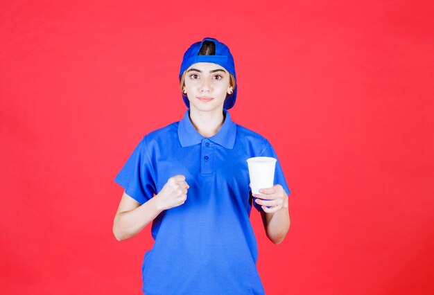 Agente de servicio femenino en uniforme azul sosteniendo un vaso desechable de bebida y mostrando su puño.
