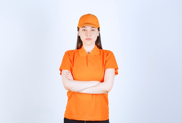 Agente de servicio femenino con uniforme de color naranja, cruzando los brazos y aspecto profesional.