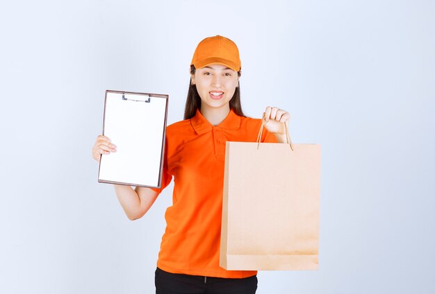 Agente de servicio femenino en uniforme de color naranja sosteniendo una bolsa de cartón y presentando la lista de firmas al cliente.