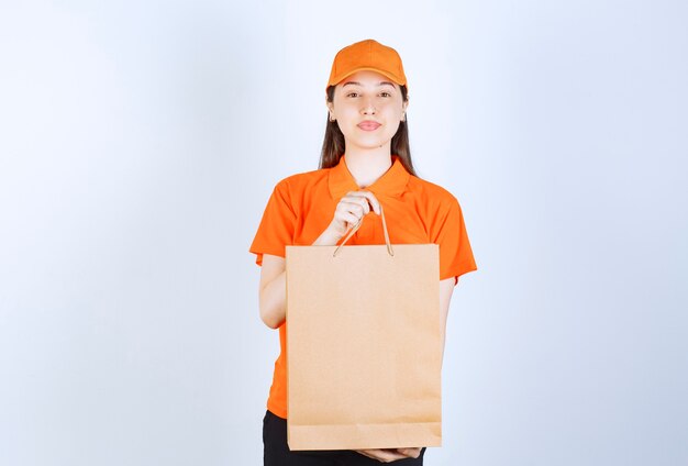 Agente de servicio femenino en uniforme de color naranja sosteniendo una bolsa de cartón y presentándola al cliente.