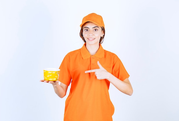 Agente de servicio femenino en uniforme naranja sosteniendo una taza amarilla para llevar