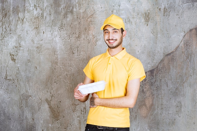 Agente de servicio masculino en uniforme amarillo sosteniendo una caja de comida para llevar blanca.