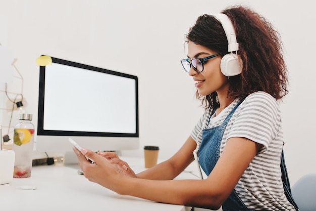 Agraciada joven con sonrisa juguetona con teléfono mirando la pantalla con interés