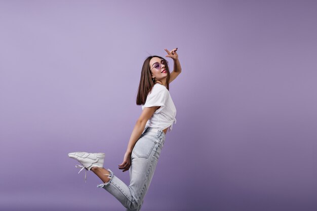 Agraciada mujer europea en zapatillas de moda divirtiéndose. Retrato de niña bonita blanca en jeans aislado.