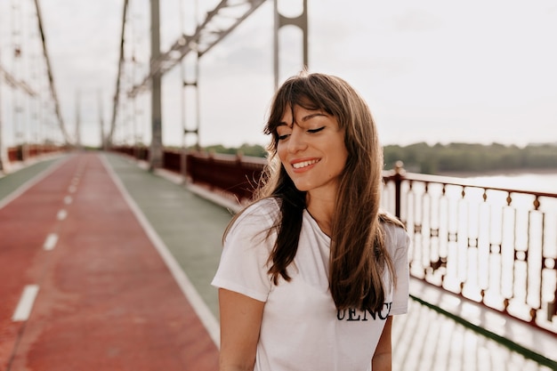 Agraciada mujer joven con cabello largo posando con gusto mientras camina afuera de buen humor.