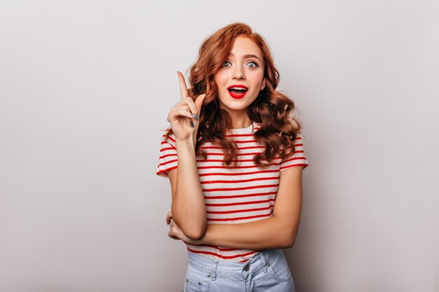 Agradable chica blanca en ropa casual posando con sonrisa de sorpresa. Atractiva mujer rizada que expresa asombro.