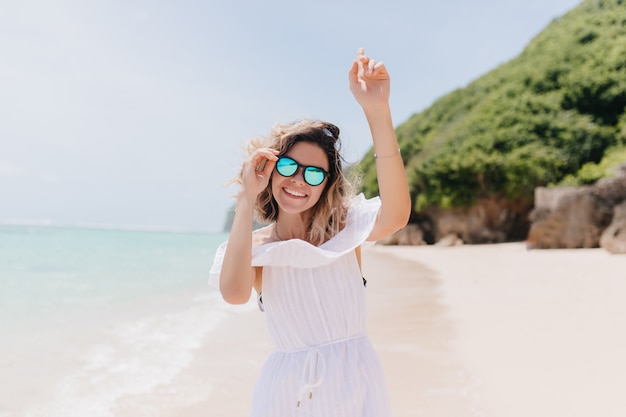 Agradable joven bailando en la isla tropical y sonriendo. Retrato al aire libre de mujer inspirada con peinado corto divirtiéndose en el resort.