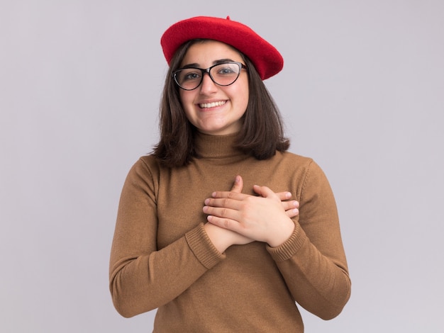 Foto gratuita agradable joven bastante caucásica con sombrero de boina y gafas ópticas pone las manos en el pecho