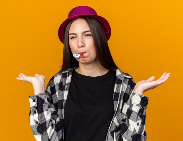 Agradable joven hermosa mujer vistiendo gorro de fiesta soplando silbato de fiesta extendiendo las manos