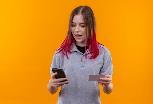 Agradable joven hermosa vestida con camiseta gris número de marcación en el teléfono sobre fondo amarillo aislado