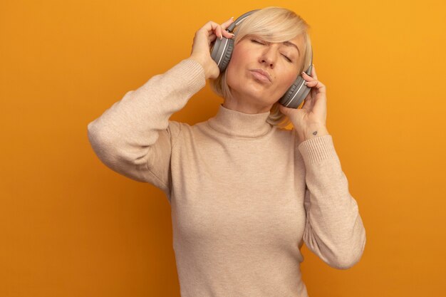 Agradable mujer eslava rubia bonita en auriculares se encuentra con los ojos cerrados en naranja