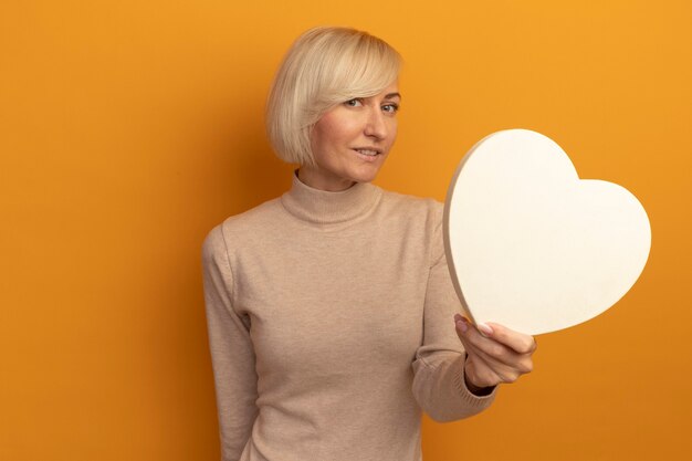 Agradable mujer eslava rubia bonita tiene forma de corazón mirando al frente aislado en la pared naranja