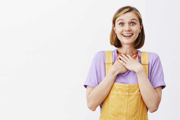 Agradecida, feliz y conmovida joven cogidos de la mano en el corazón y sonriendo agradecido, recibir la oportunidad