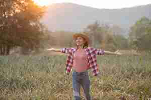 Foto gratuita la agricultora asiática ve el crecimiento de la piña en la granja, mujer joven bonita del granjero de pie en tierras de cultivo con los brazos levantados hacia la alegría eufórica alegría.