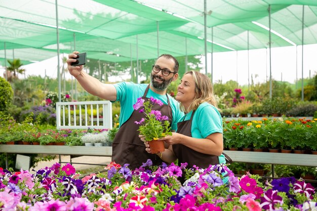 Agricultores felices tomando selfie con planta floreciente de petunia
