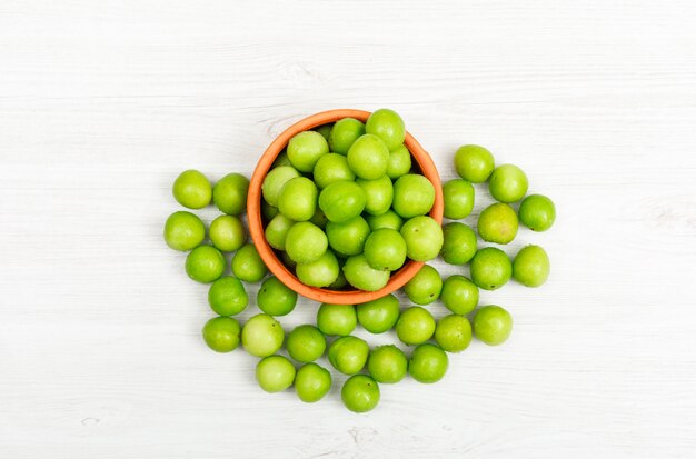 Agrie las ciruelas verdes en un tazón hecho a mano en una madera blanca. vista superior.