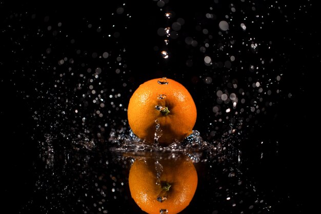 El agua chispeante cae en naranja rojo jugoso que se encuentra en la mesa de negro