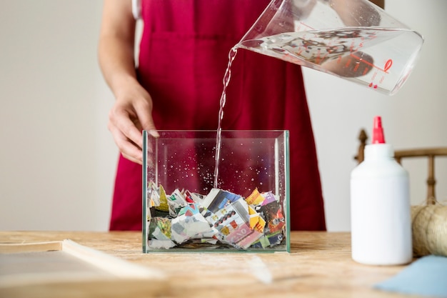 Agua de colada femenina en el recipiente lleno de papel en el escritorio de madera