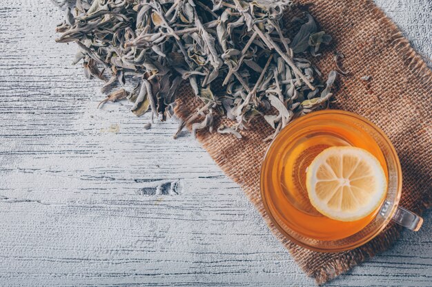 Agua de color naranja con vista superior de hierbas de té sobre una tela de saco y fondo de madera gris. espacio para texto