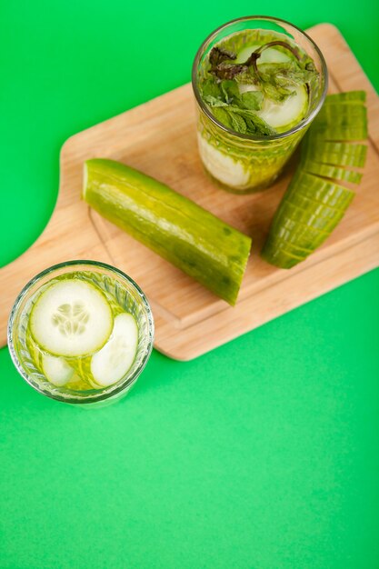 Agua de desintoxicación casera de pepinos orgánicos en un vaso sobre un fondo verde