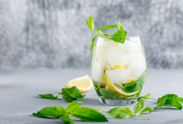 Agua de desintoxicación helada con limón y menta en un vaso sobre superficie gris y grunge
