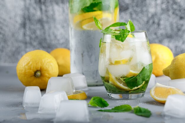 Agua de desintoxicación helada con limones, menta en vidrio y botella sobre superficie gris y sucia