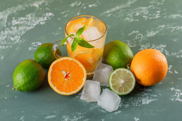 Agua de desintoxicación helada en una taza con naranjas, menta, limas, vista de ángulo alto sobre una superficie de yeso