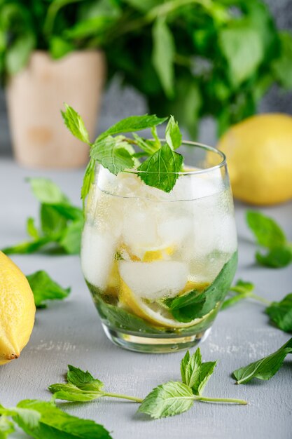 Agua de desintoxicación helada en un vaso con limones y primer plano de menta en superficie gris y grunge