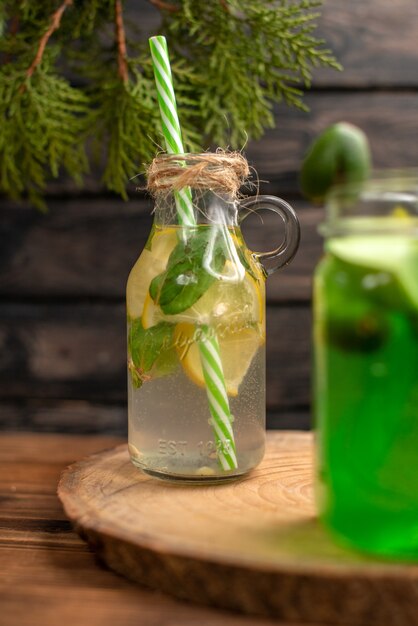 Agua de desintoxicación y jugo fresco en botellas con tubos sobre fondo de madera marrón