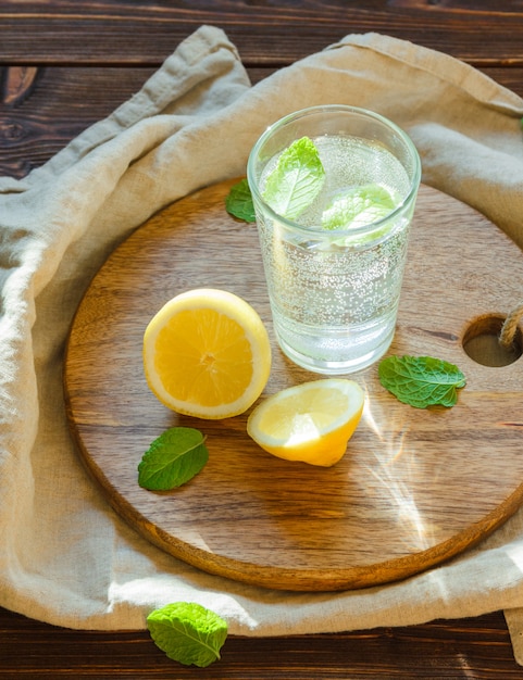 Agua con gas en vidrio con tabla de cortar, hojas y limón.