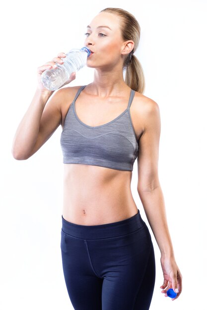 Agua potable hermosa joven después de hacer ejercicio sobre fondo blanco.