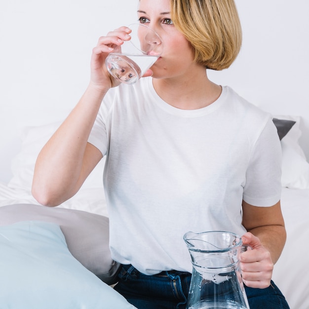 Agua potable de mujer cerca de almohadas