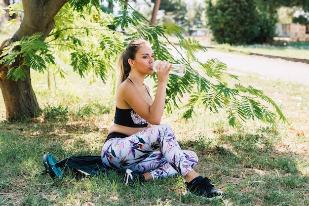 Agua potable de la mujer joven de la aptitud de la botella en el parque