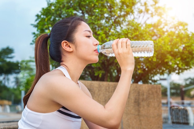 Agua potable de mujer joven deportiva después de trotar.