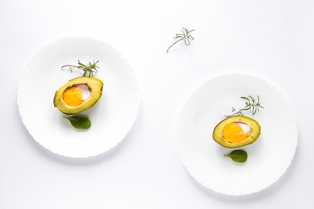 Aguacate al horno con huevo en un plato sobre fondo blanco