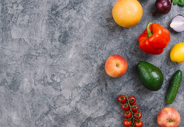 Aguacate; Pimiento; naranja; manzana; Pepino; Tomates limón y cereza sobre fondo de hormigón con textura