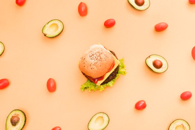 Aguacate y tomates cherry rodeados alrededor de la hamburguesa sobre fondo coloreado