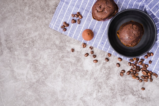 Foto gratuita ahueque la torta de la taza y los granos de café asados ​​en servilleta sobre el fondo concreto