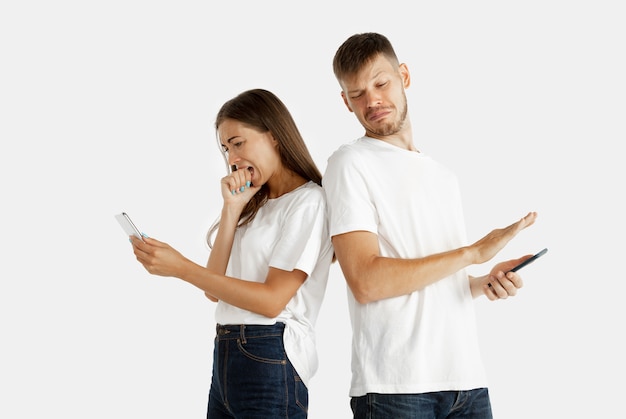 Aislado retrato de la hermosa joven pareja. Expresión facial, emociones humanas. Hombre y mujer sosteniendo teléfonos inteligentes y miran asustados de su pantalla.