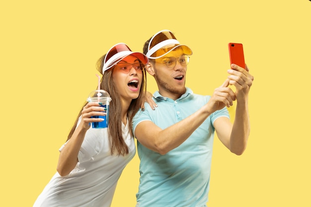 Aislado retrato de medio cuerpo de la hermosa joven pareja. Mujer y hombre de pie con bebidas haciendo selfie. Expresión facial, verano, concepto de fin de semana. Colores de moda.