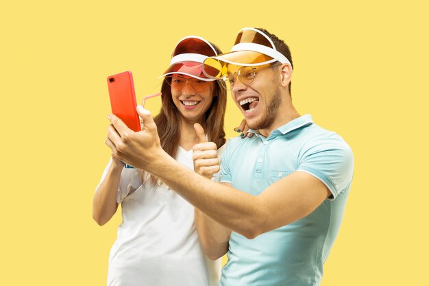 Aislado retrato de medio cuerpo de la hermosa joven pareja. Mujer y hombre de pie con bebidas haciendo selfie. Expresión facial, verano, concepto de fin de semana. Colores de moda.