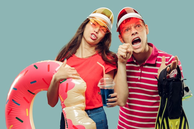 Aislado retrato de medio cuerpo de la hermosa joven pareja. Sonriente mujer y hombre con gorras y gafas de sol con equipo de natación. Expresión facial, verano, concepto de fin de semana.