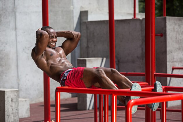 ajuste atleta haciendo ejercicios en el estadio. Hombre afro al aire libre en la ciudad. Tire hacia arriba de los ejercicios deportivos.