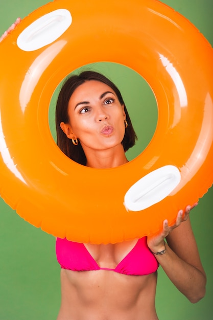 Foto gratuita ajuste de verano mujer deportiva en bikini rosa y anillo inflable de color naranja brillante redondo en verde, feliz juguetón con muecas divertidas